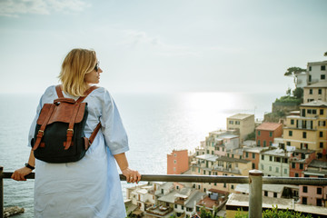 Woman in casual dress with backpack looking to sea. Travel Cinque Terre in Italy in summer