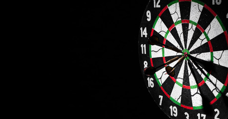 Dartboard with dart arrow hitting the center on a dark black background with copy space.