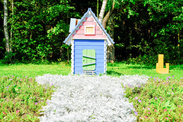 A wooden fairy-tale toy house in green grass in the sun. The concept of 