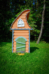 A wooden fairy-tale toy house in green grass in the sun. The concept of 