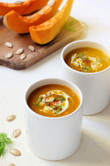 Roasted pumpkin and carrot soup with cream and pumpkin seeds on two white mug on white background with black bread slices.Vegetarian eating.Diet and healthy food concept.Space for copy and text