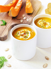 Roasted pumpkin and carrot soup with cream and pumpkin seeds on two white mug on white background with black bread slices.Vegetarian eating.Diet and healthy food concept.Space for copy and text