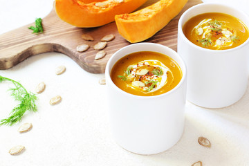 Roasted pumpkin and carrot soup with cream and pumpkin seeds on two white mug on white background with black bread slices.Vegetarian eating.Diet and healthy food concept.Space for copy and text