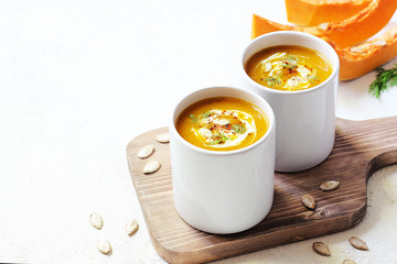 Roasted pumpkin and carrot soup with cream and pumpkin seeds on two white mug on white background with black bread slices.Vegetarian eating.Diet and healthy food concept.Space for copy and text