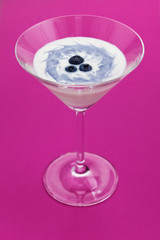 Vertical photo of fresh yogurt with blueberries in a glass on pink background.