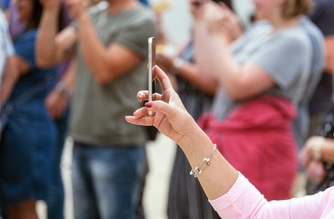 Frau fotografiert und filmt in einer Gruppe, mit ihrem Smartphone bei einer Ã¶ffentlichen...