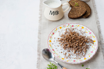 Traditional Russian food. Buckwheat porridge with milk and black bread on the table. Horizontal orientation.