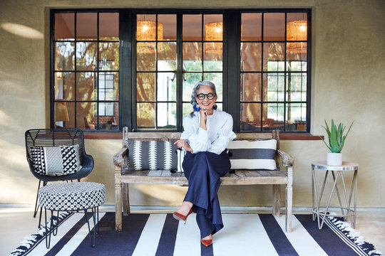 Portrait of beautiful and stylish mature woman interior designer with grey hair sitting on front porch