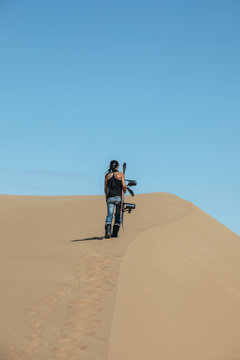 tattoed sporty woman walking up a dune with her snowboard