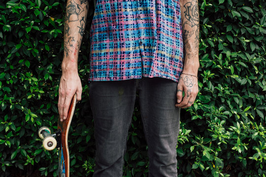 Close up of skaters hand holding a skateboard against the green bush background