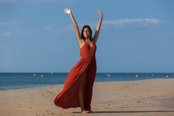 Fototapeta na wymiar Pretty young woman in a red dress and nude foots on the sand of the beach. Happy girl enjoying freedom at the sea..