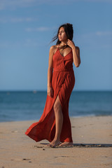 Fototapeta na wymiar Pretty young woman in a red dress and nude foots on the sand of the beach. Happy girl enjoying freedom at the sea..