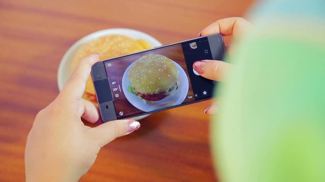 Female hands hold the phone and take a picture of a burger.