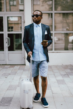 Black man with suitcase using smartphone