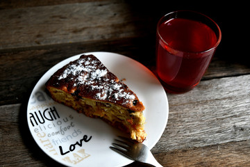 Charlotte on a white plate, fork and compote of apples on a wooden table.