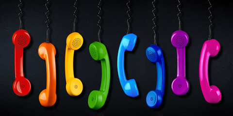 row of colorful rainbow colored old fashioned retro phone reciever with black telephone wire black...
