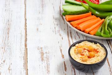 Hummus platter with assorted snacks. Hummus in bowl, vegetables sticks, chickpeas, olives. Plate with Middle Eastern/Mediterranean meze. Party/finger food. Top view. Vegetables, hummus dip,copy space