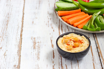 Hummus platter with assorted snacks. Hummus in bowl, vegetables sticks, chickpeas, olives. Plate with Middle Eastern/Mediterranean meze. Party/finger food. Top view. Vegetables, hummus dip,copy space