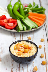 Hummus platter with assorted snacks. Hummus in bowl, vegetables sticks, chickpeas, olives. Plate with Middle Eastern/Mediterranean meze. Party/finger food. Top view. Vegetables, hummus dip,copy space