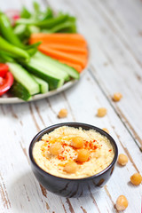 Hummus platter with assorted snacks. Hummus in bowl, vegetables sticks, chickpeas, olives. Plate with Middle Eastern/Mediterranean meze. Party/finger food. Top view. Vegetables, hummus dip,copy space