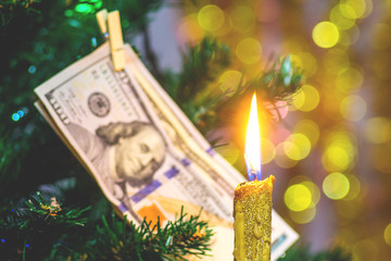 Candle near the Christmas tree, decorated with a hundred dollar bill. Wealth in the New Year_