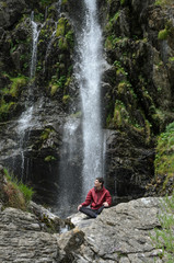 Wet young man posing in front of a waterfall