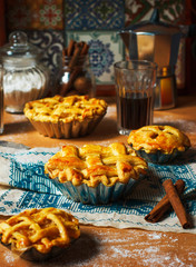 Mini homemade apple pies on rustic background with coffee,cinnamon sticks,apples,vintage towel