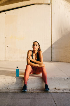 Beautiful sportswoman sitting on pavement