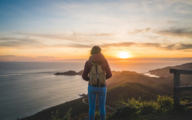 Girl traveler watching a beautiful sunset over the Pacific Ocean on top of a hill