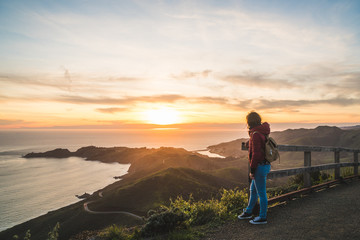 Girl solo traveler watching a beautiful sunset over the Pacific Ocean on top of a hill