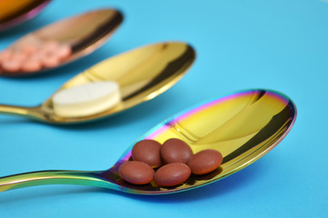 Three different types of pills in three colored shine metal spoons on blue background
