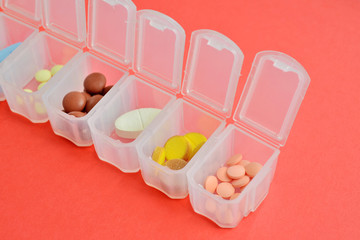 Plastic daily organizer for pills, box with different pills on pink background with copyspace