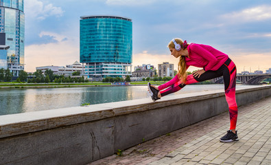 white girl athlete doing workout on embankment of the megapolis river with business buildings in the background