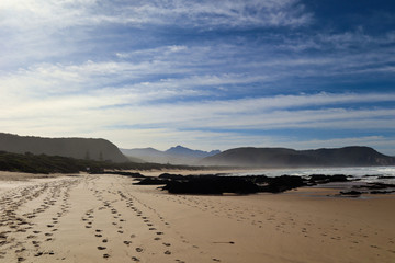 Footprints in the sand, and a view of coast and mountains.