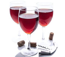 Three glasses with red wine, corkscrew and cork on a white background. Isolated composition