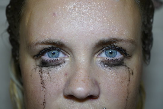 Flowed mascara on the blue eyes of the girl. Wet girl with leaking mascara in front of her eyes. Face close up.