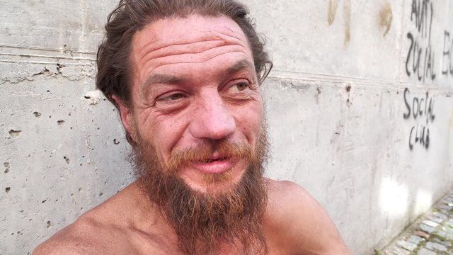 Down-and-out person talks on the camera. Homeless man looks at the camera and talks. Real person with no fixed abode close up