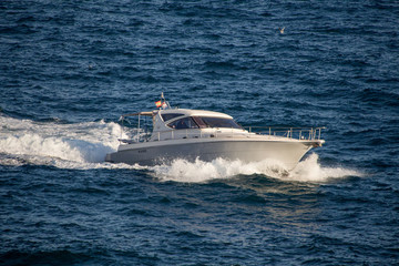 Small white yacht in Spanish sea with blue water creating waves.