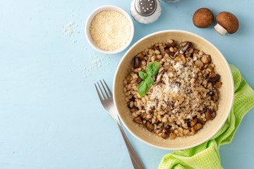 Pearl barley risotto or orzotto with mushrooms and parmesan cheese in bowl on blue concrete background. Top view. Copy space.