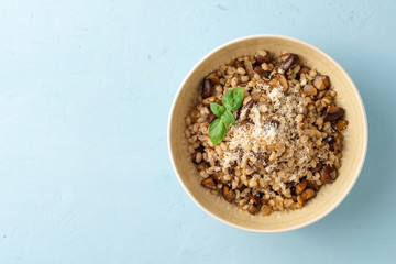 Pearl barley risotto or orzotto with mushrooms and parmesan cheese in bowl on blue concrete background. Top view. Copy space.