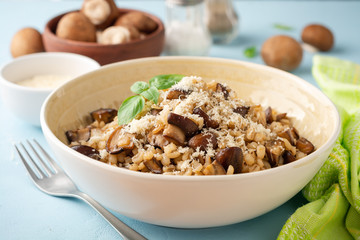 Pearl barley risotto or orzotto with mushrooms and parmesan cheese in bowl on blue concrete background. Selective focus.