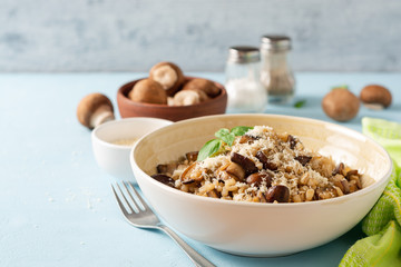 Pearl barley risotto or orzotto with mushrooms and parmesan cheese in bowl on blue concrete background. Selective focus.