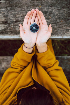 From above anonymous female holding small vintage compass in hands over wooden table during trip in countryside