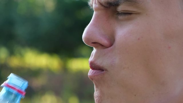 Man with increased tooth sensitivity drinking water on nature background, close up