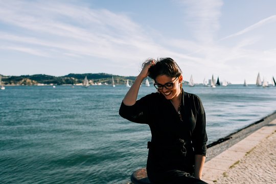 Side view of young attractive woman in black outfit standing by sea and leaning on pole in Lisbon