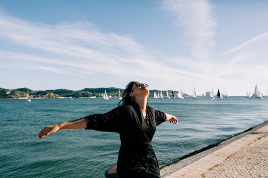 Side view of young attractive woman in black outfit standing by sea and leaning on pole in Lisbon