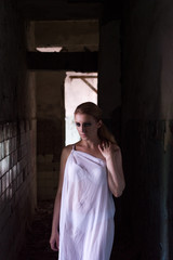 Girl in white clothes in a dark corridor. Beautiful girl in a scary room.