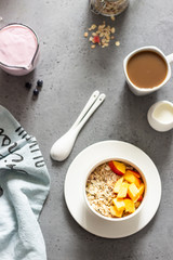 Ceramic bowl with crunchy granola served with peaches, a cup of coffee with milk, jar with granola and berry yogurt. Breakfast concept.