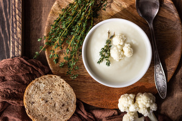 Wooden tray with two ceramic bowl with cauliflower cream soup garnish with fresh cauliflower, thyme...