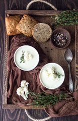 Wooden tray with two ceramic bowl with cauliflower cream soup garnish with fresh cauliflower, thyme and bread. Autumn or winter comfort food. 